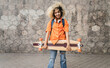 © Westend61 - Smiling woman holding skateboard standing in front of wall
