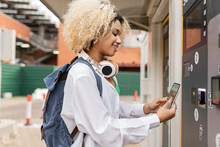Smiling Woman Scanning QR Code Through Smart Phone On Ticket Vending Machine