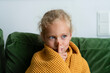 © Westend61 - Contemplative girl wrapped in blanket making silence gesture at home