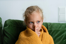 Contemplative Girl Wrapped In Blanket Making Silence Gesture At Home