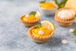 Mini tarts with lemon curd, mini meringue, lemon slices and mint, blue concrete background.