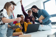 © Halfpoint - High school students sitting together at desk and using laptop and talking during break in classroom.