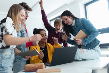 Wall Mural - high school students sitting together at desk and using laptop and talking during break in classroom