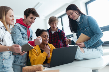 Wall Mural - high school students sitting together at desk and using laptop and talking during break in classroom
