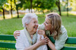 © Halfpoint - Adult granddaguhter helping her grandmother to use cellphone when sitting on bench in park in summer.