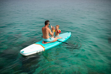 Wall Mural - Happy father and little son on paddle board in sea together. Fatherhood and quality time with child concept.