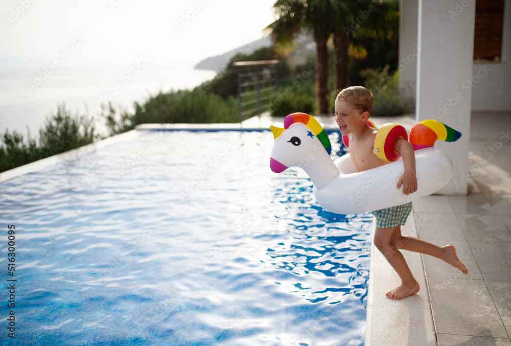 Happy kid having fun when jumping to swimming pool with inflatable ring ...
