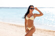 © Syda Productions - people, summer and swimwear concept - happy smiling young woman in bikini swimsuit and sunglasses posing on beach
