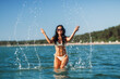 © Syda Productions - people, summer and swimwear concept - happy smiling woman in bikini swimsuit splashing sea water on beach