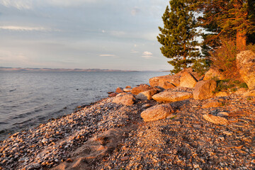 Wall Mural - Baikal Lake on a summer morning. A beautiful landscape with a rocky shore of the Small Sea and green trees at the golden hour at dawn. Natural background. Travel and recreation on the lake