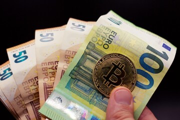 Hand holding a bitcoin and Euro bills, concept of new crypto currency.