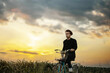 © velimir - young man rides a bicycle across a field in a village at sunset. Romantic retro bike ride