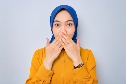 Shocked young Asian Muslim woman dressed in orange covering mouth with hand for mistake isolated over white background