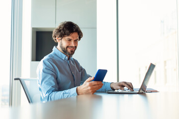 Poster - Cheerful mature businessman checking smartphone, using laptop computer, working online at company office