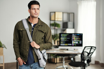 Portrait of young ambitious software developer with cross body bag standing in office and looking away