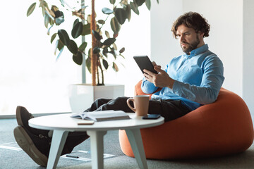 Poster - Focused mature entrepreneur using digital tablet at workplace, sitting in bean bag chair at office, copy space