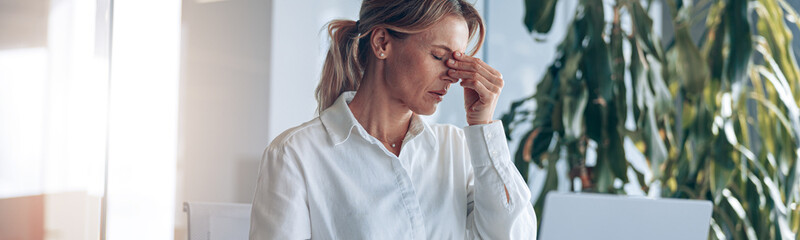 Wall Mural - Tired lady boss with headache working on laptop at workplace in modern office. Business concept.
