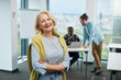 © chika_milan - A happy female senior student is standing in a classroom with arms crossed and smiling at the camera. A woman successfully finished the course.