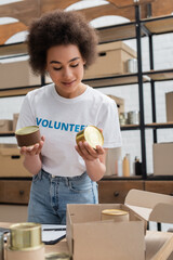 Sticker - african american volunteer holding canned food in donation storehouse.