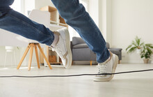 Clumsy Person Falls Down After Stumbling Over A Power Cable. Man Or Woman In Sneakers Trips Over An Electrical Cord While Walking On The Floor At Home. Cropped Shot. Domestic Accident Concept