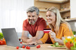 © Prostock-studio - Cheerful couple making online order, using laptop at kitchen