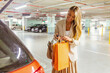© Jelena Stanojkovic - A young woman packs a shopping bag in the trunk of a car, she is happy with the purchase. A young woman carries shopping bags, walks towards her car and smiles.
