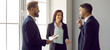 © Studio Romantic - Team of business people talking. Group of three happy colleagues discussing work standing together by the office window. Young man and woman enjoying a conversation with a more experienced coworker