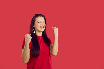 Overjoyed young woman isolated on red studio background feel excited make yes gesture. Smiling female triumph celebrate win or victory. Girl euphoric with success. Luck concept.