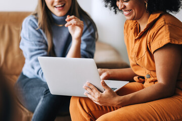 Wall Mural - Cheerful businesswomen using a laptop together in an office lobby