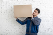 © Vitaliy - Handsome man from moving service carrying heavy box in front of white brick wall background