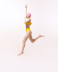 Portrait of young woman in swimming suit and cap jumping with nose covered into water isolated over grey studio background