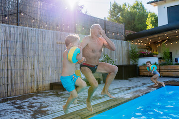 Wall Mural - Grandfather with his granson having fun together when jumping into the swimming pool at backyard.