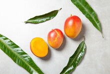 Top View Of Two And Half Mangos With Four Green Leaves On A Granite Background