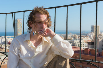 Young man sitting on a rooftop with a city in the background