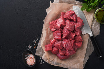 Wall Mural - Raw chopped beef meat. Raw organic meat beef or lamb, spices, herbs on old parchment paper on dark grey concrete background. Goulash. Raw uncooked meat. Meat with blood. Top view with copy space.