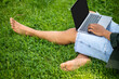 Legs of man sitting on grass with laptop