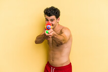 Young Caucasian Man Playing With A Water Gun Isolated On Yellow Background