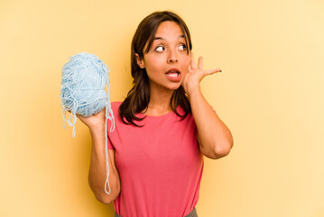 Wall Mural - Young hispanic woman holding a ball of wool isolated on yellow background trying to listening a gossip.