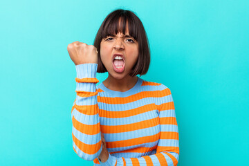 Wall Mural - Young mixed race woman isolated on blue background showing fist to camera, aggressive facial expression.