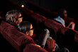 © Seventyfour - Rear view of young couple watching 3d movie in glasses on comfortable armchairs in cinema
