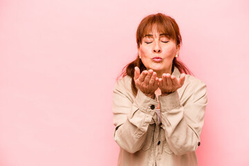 Wall Mural - Middle age caucasian woman isolated on pink background folding lips and holding palms to send air kiss.