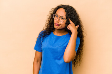 Young hispanic woman isolated on beige background pointing temple with finger, thinking, focused on a task.