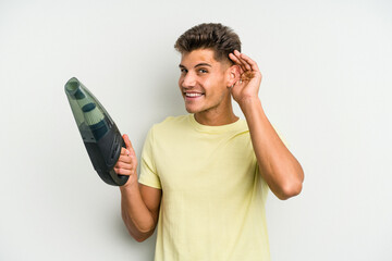 Poster - Young caucasian man holding a hand vacuum cleaner isolated on white background trying to listening a gossip.