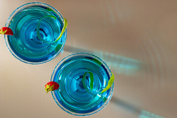 Wall Mural - Two glasses with blue margarita cocktail garnished with lime zest and strawberries, selective focus