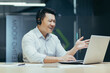 © Liubomir - Angry and annoyed asian businessman with headset for video call, talking in online meeting, looking at laptop screen, man at work