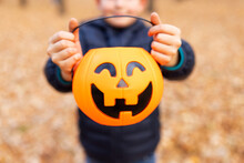Child Holds A Bucket Shaped Like A Halloween Pumpkin Jack O Lantern In Autumn Park. Kid With Jack-o-lantern. Halloween - Traditional American Holiday
