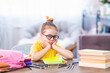 Cute thoughtful tired schoolgirl with glasses. Sitting at his desk at home and bored. Back to school. Little girl C does not want to get knowledge and do homework. Learning problems