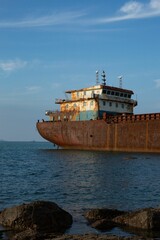 Sticker - Vertical shot of an abandoned rusty ship on a tranquil sea captured from a rocky shore