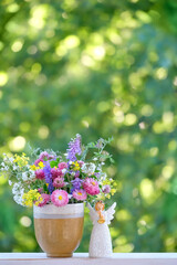 Poster - Beautiful angel and bouquet of wild flowers in cup on table, abstract natural background. Religious church holiday. symbol of faith in God, christianity. Happy Name Day greeting card concept.