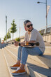 © Julija - Man sit with skateboard in city landscape.beard guy with skateboard sitting on the street smiling happy.